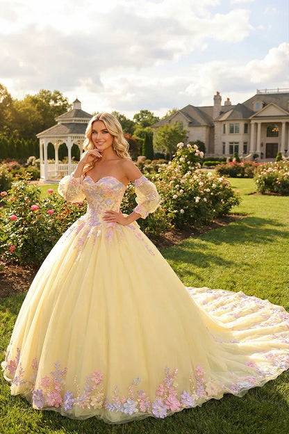 Woman in a yellow ball gown with floral lace and sheer long sleeves in a garden