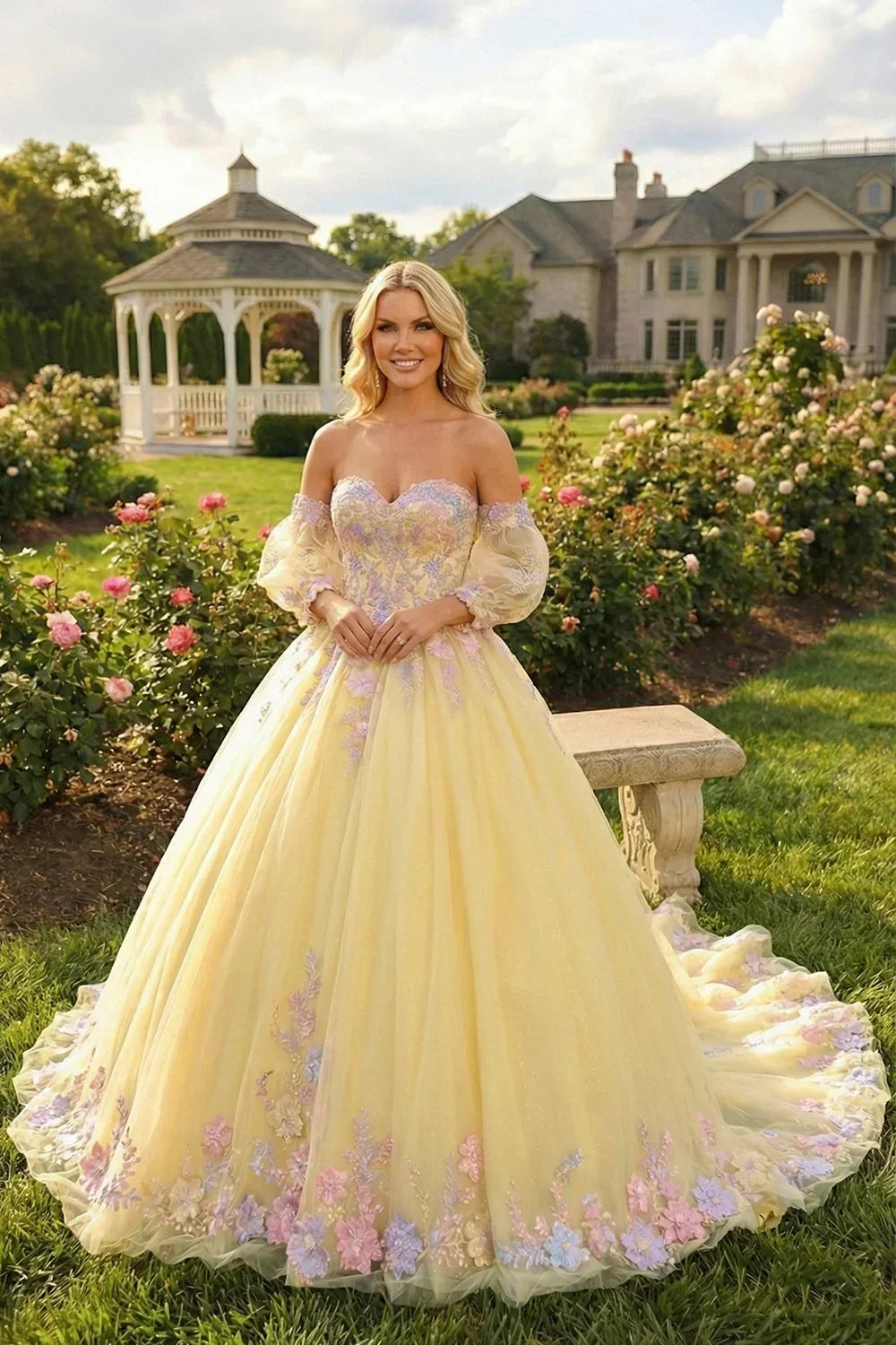 Woman in yellow ball gown with floral lace, cold shoulder and sheer long sleeves in garden