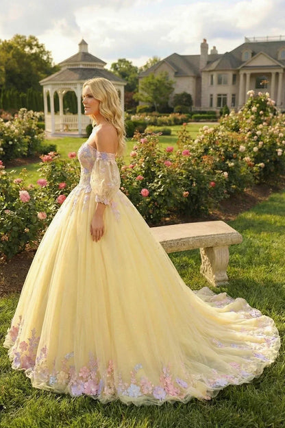 Woman in a yellow off-shoulder ball gown with floral lace details in a garden setting