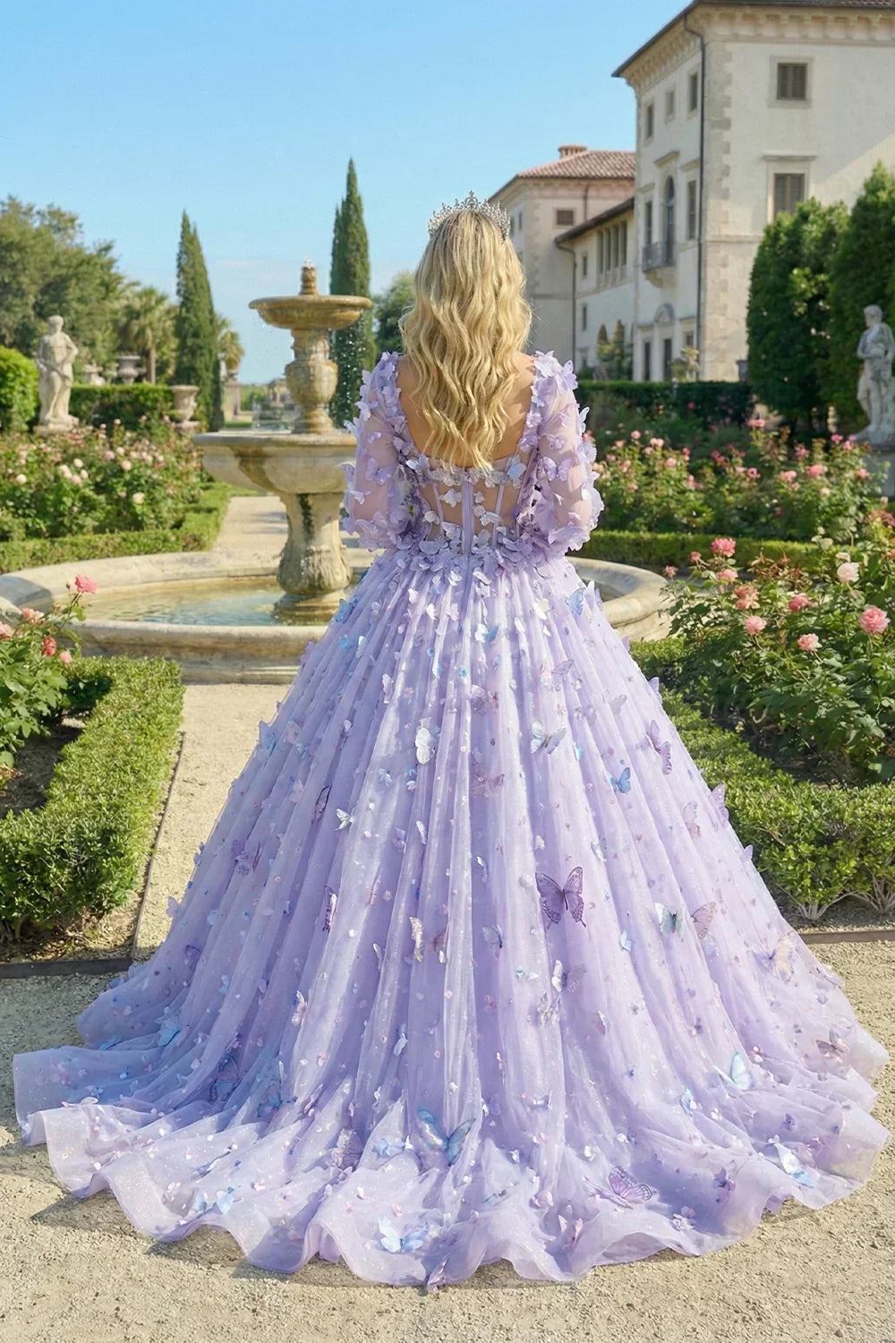 Back view of a woman in a lavender ball gown with 3D butterfly appliqués and long illusion sleeves in a formal garden setting.