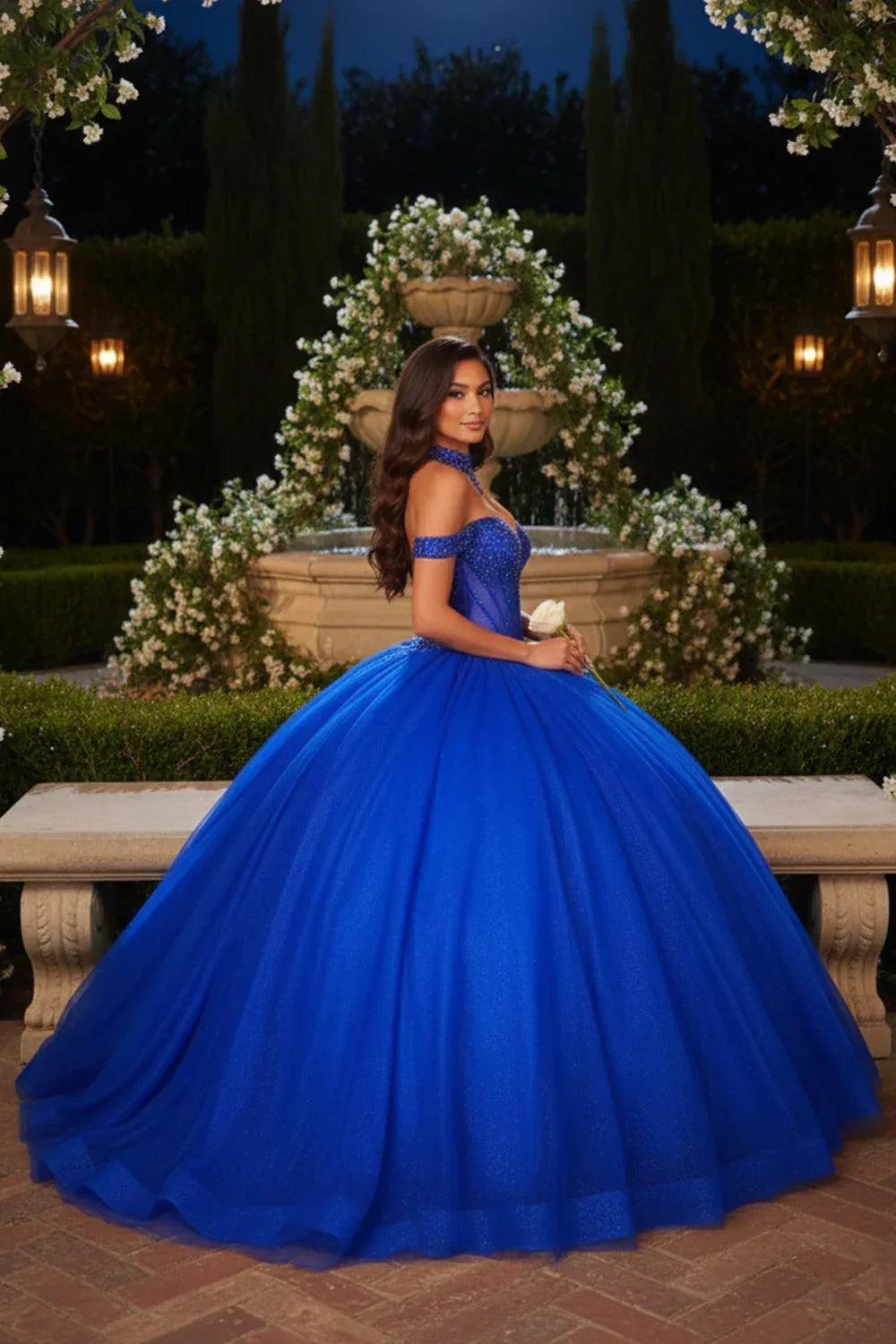 Woman in royal blue off-the-shoulder ball gown posing by garden fountain at night