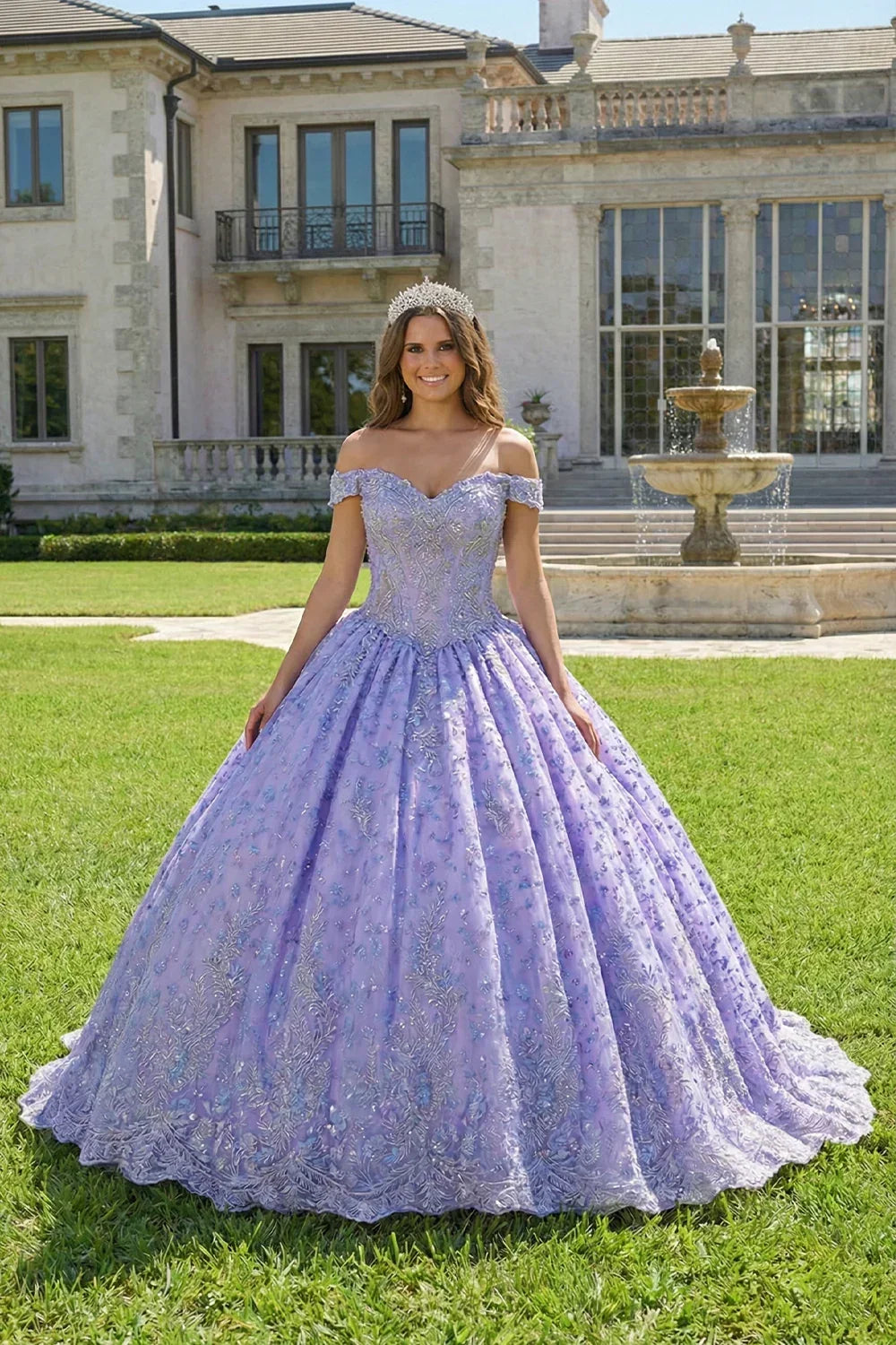 Woman in a lilac ball gown with floral embroidery and off-the-shoulder sleeves outside a mansion.
