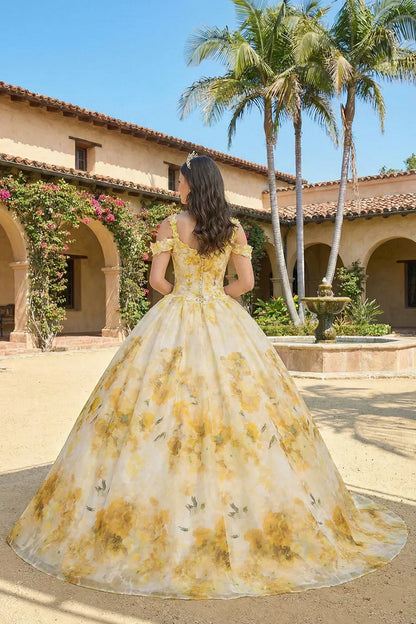 Elegant yellow floral ball gown with spaghetti straps, worn outdoors by a fountain.