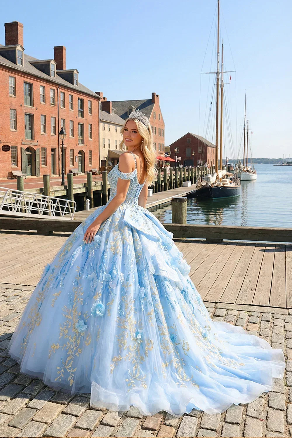 Woman in a blue glittery ball gown with gold embroidery and floral appliqués, outdoor harbor scene