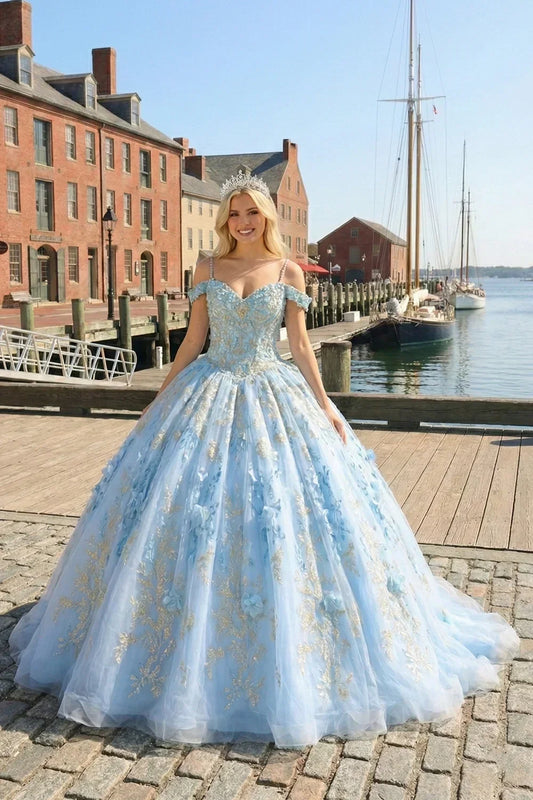 Woman in a blue glittery ball gown with 3D floral details and embroidery, standing by a harbor.