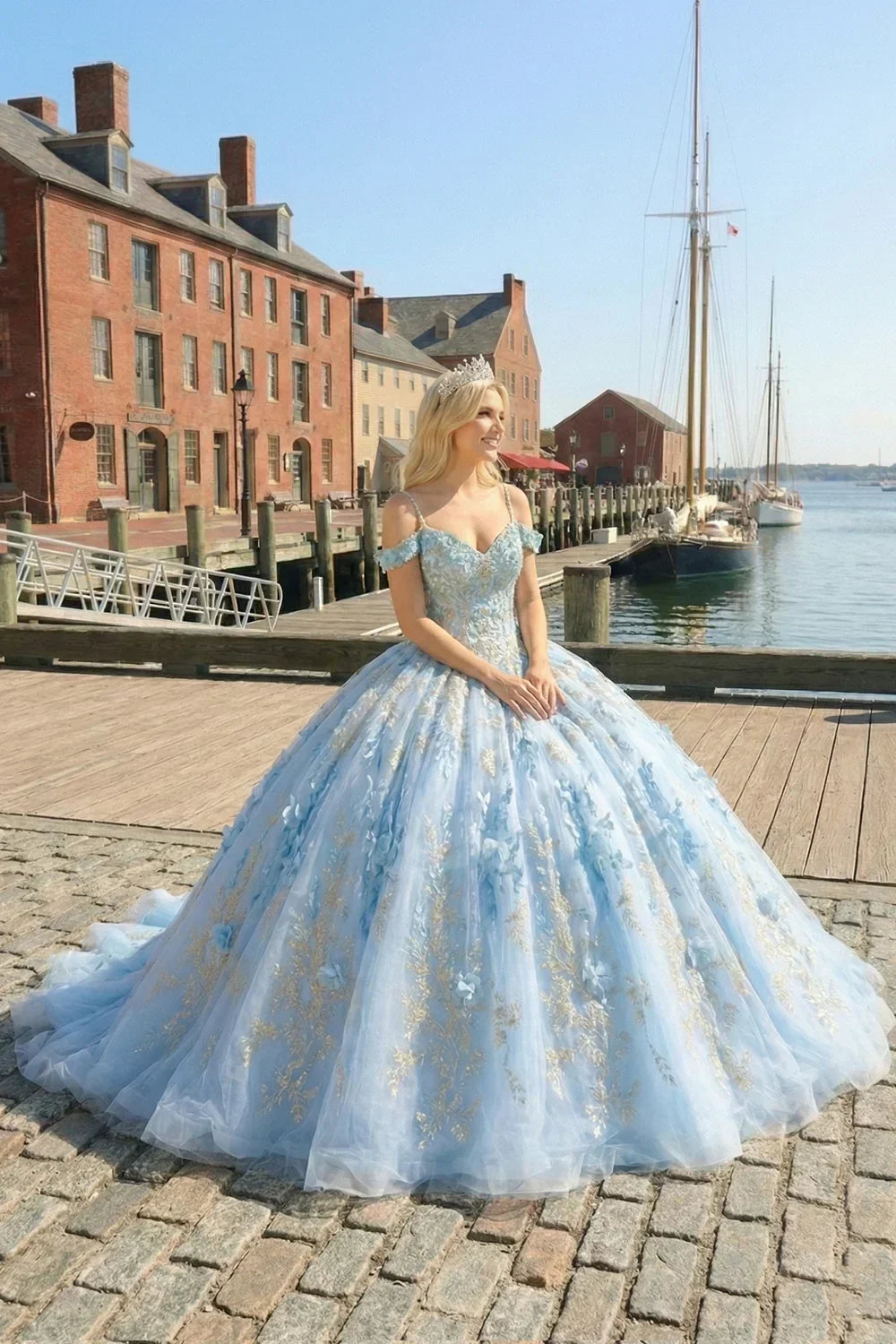 Woman in a glittery blue ball gown with floral embroidery and tiara by a waterfront