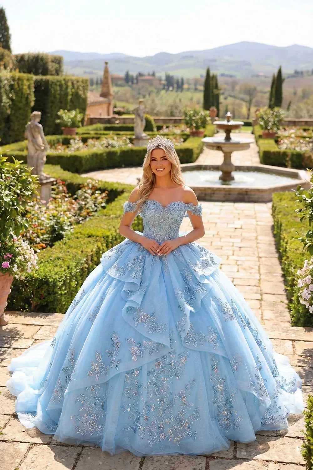 Woman in a blue layered ruffled ball gown with embroidery and tiara in a formal garden