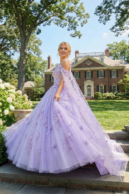 Woman in a lavender ball gown with 3D floral details and a sheer cape, outdoors by a mansion