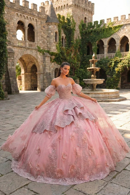Woman in a pink embroidered ruffle ball gown with 3D floral details, posing in a castle courtyard