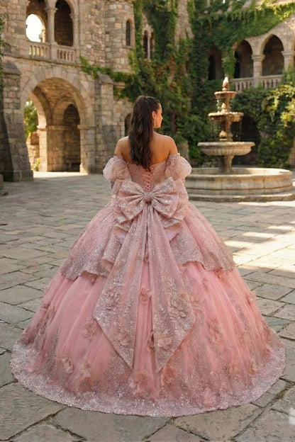 Pink textured ruffle ball gown with floral embroidery and large bow in a castle courtyard